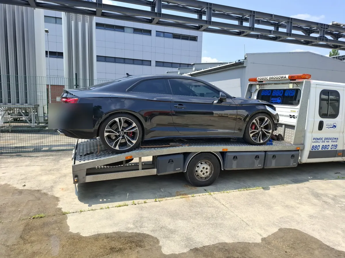 Czarne Audi S5 na platformie lawety przy hali